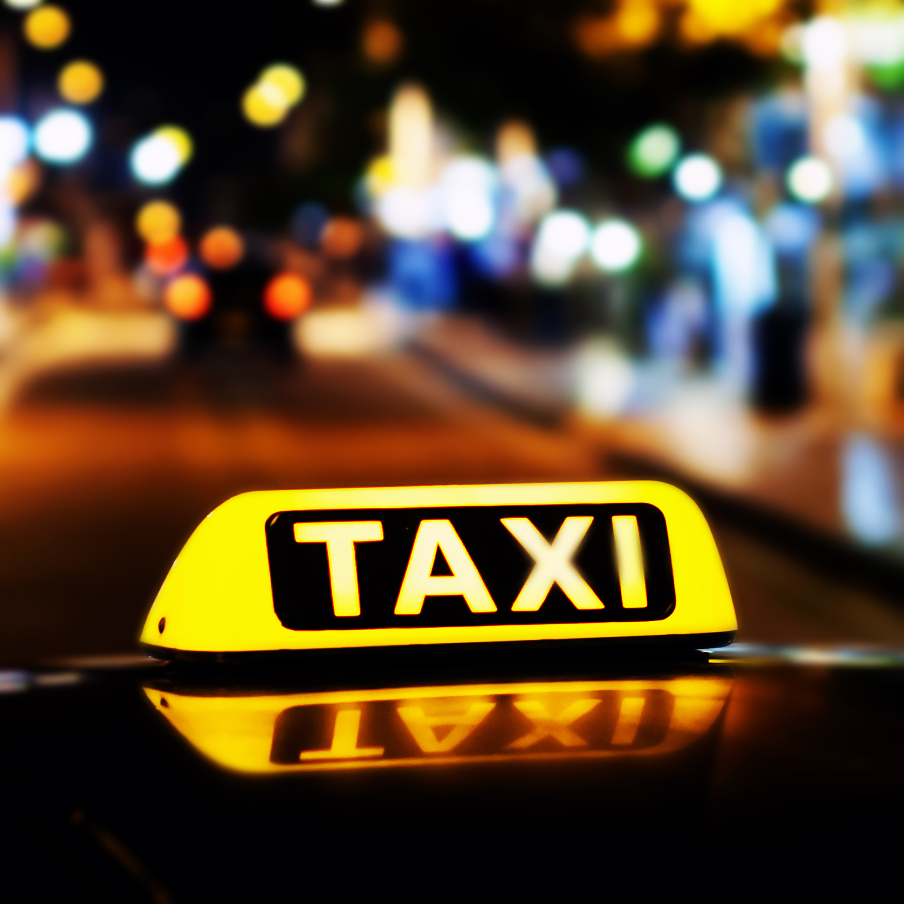 Leuchtendes gelbes Taxi-Schild auf einem Fahrzeug vor nächtlichem unscharfen Hintergrund.