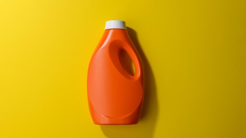 Orangefarbene Waschmittelflasche vor gelb-olivfarbenem Hintergrund
